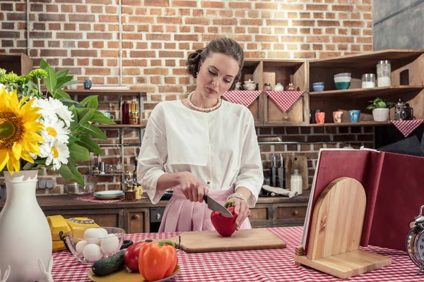 Концентрированная взрослая домохозяйка режет красный перец на кухне — стоковое фото