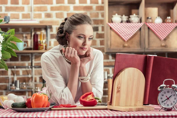 Attractive adult housewife in vintage clothes reading recipe book at kitchen — Stock Photo