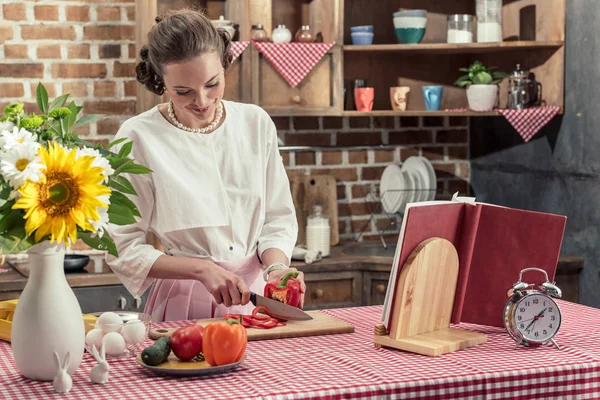 Smiling adult housewife cutting bell pepper at kitchen — Stock Photo