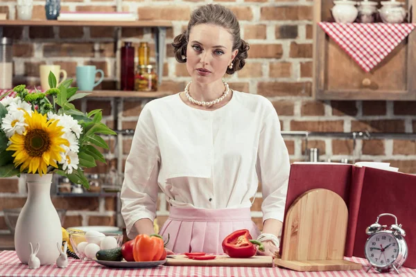 Красивая взрослая домохозяйка в винтажной одежде смотрит в камеру на кухне — стоковое фото