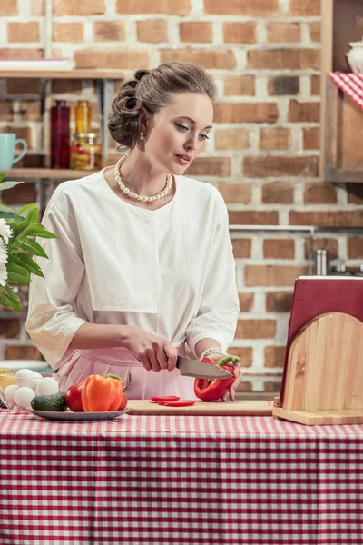 Élégante femme au foyer adulte en vêtements vintage couper la tomate à la cuisine — Photo de stock