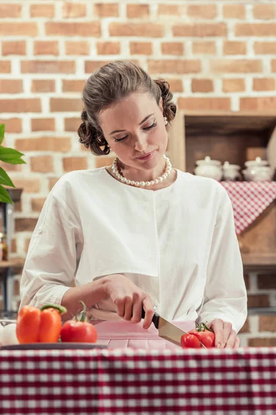 Attractive adult housewife in vintage clothes cutting tomato at kitchen — Stock Photo