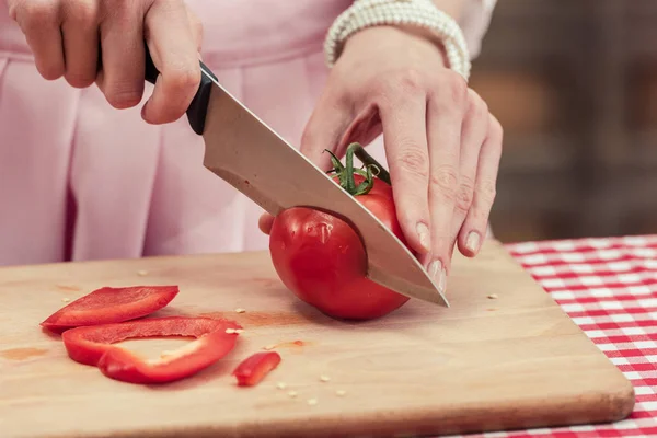 Cropped shot of housewife cutitng tomato on wooden cutting board — Stock Photo