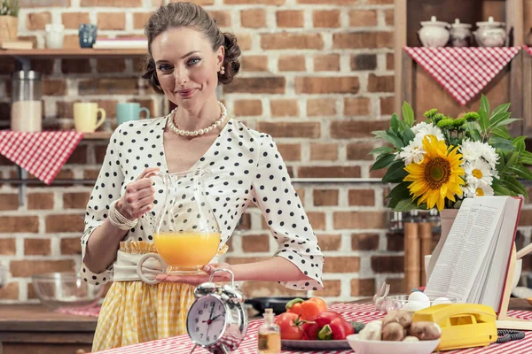 Sorrindo adulto dona de casa segurando jarro de suco de laranja e olhando para a câmera na cozinha — Fotografia de Stock