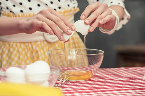 Recortado tiro de ama de casa en polka punto camisa romper el huevo en tazón para tortilla - foto de stock