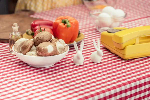 Primer plano de teléfono vintage con varias verduras y conejitos de porcelana en la mesa - foto de stock