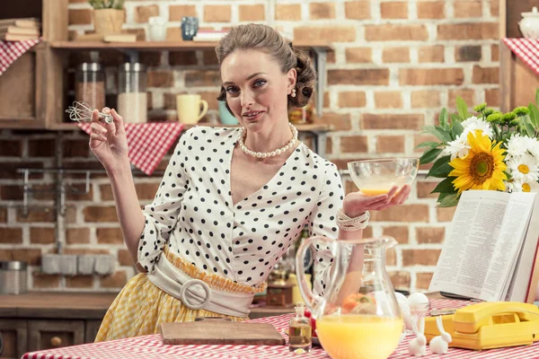 Heureuse femme au foyer adulte avec bol en verre et fouet regardant la caméra à la cuisine — Photo de stock