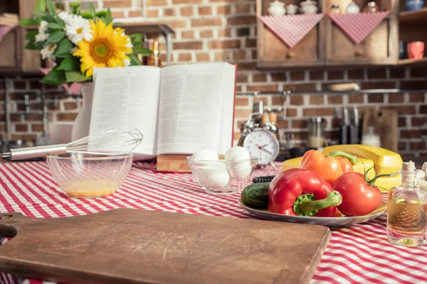 Различные сырые продукты и рецепт книги по приготовлению стола на кухне — стоковое фото