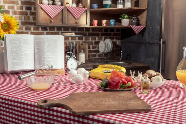 Various uncooked products and recipe book on cooking table at kitchen — Stock Photo