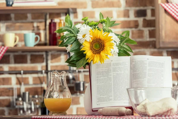Libro de recetas y ramo de flores en la mesa de cocina en la cocina - foto de stock