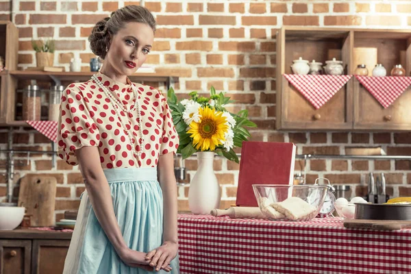 Attractive adult housewife in vintage clothes looking at camera at kitchen — Stock Photo