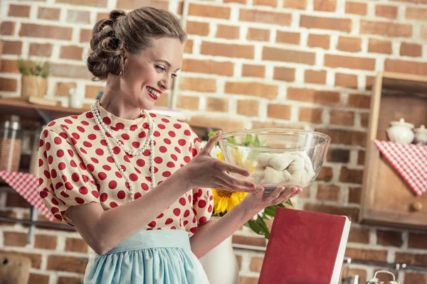 Heureuse femme au foyer adulte regardant la pâte dans un bol en verre à la cuisine — Photo de stock