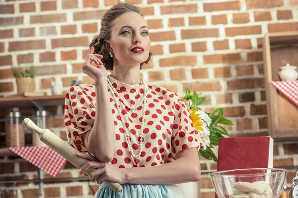 Thoughtful adult housewife with rolling pin looking away at kitchen — Stock Photo