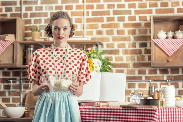 Bela dona de casa adulta segurando tigela de massa e olhando para a câmera na cozinha — Fotografia de Stock