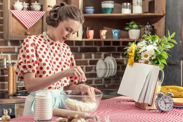 Schöne erwachsene Hausfrau verschüttet Mehl auf Teig in Schüssel in der Küche — Stockfoto