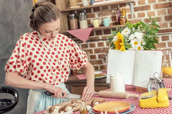 Belle femme au foyer adulte en chemise à pois coupant des champignons à la cuisine — Photo de stock