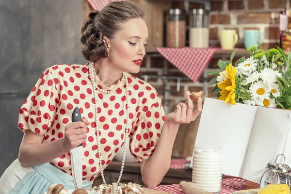 Hermosa ama de casa adulta con cuchillo mirando hongos en rodajas mientras cocina en la cocina - foto de stock