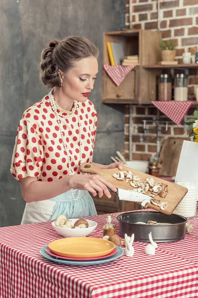 Hermosa ama de casa adulta verter setas en rodajas en hornear trey para pastel en la cocina - foto de stock