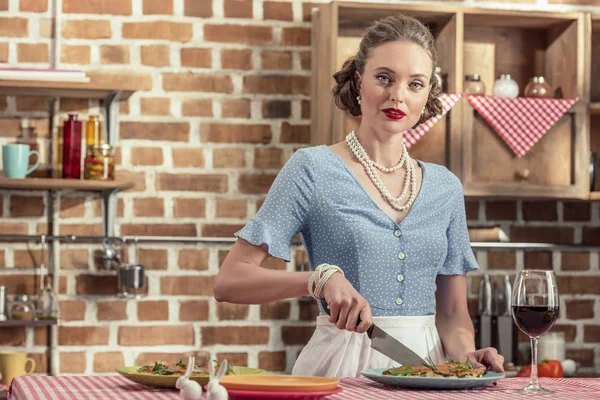 Belle femme au foyer adulte coupe gâteau aux champignons frais et regardant la caméra à la cuisine — Photo de stock