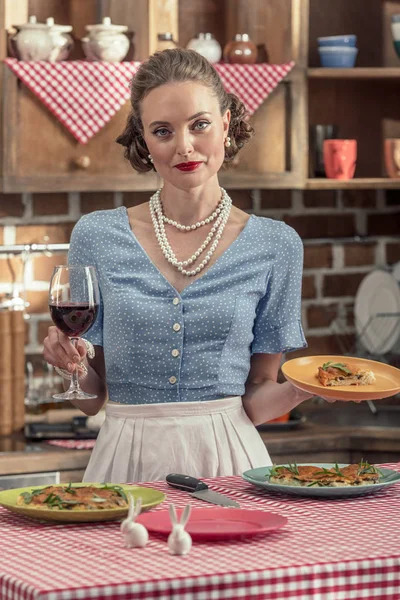 Schöne erwachsene Hausfrau mit einem Glas Rotwein und frisch gebackenem Kuchen in der Küche — Stockfoto