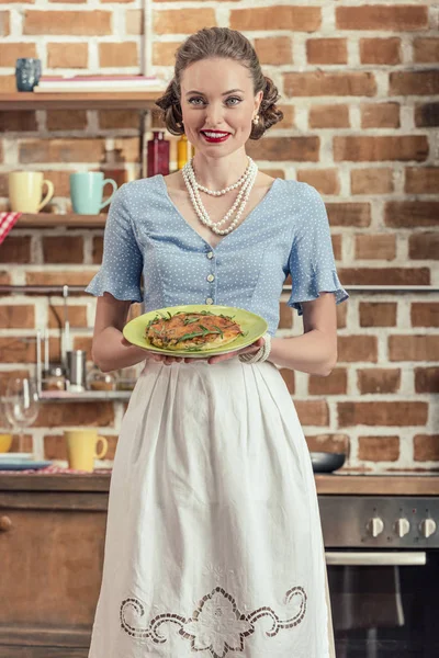 Feliz ama de casa adulta en ropa vintage placa de celebración con pastel de setas en la cocina - foto de stock