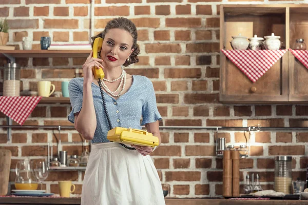 Attractive adult housewife talking by vintage rotary phone at kitchen — Stock Photo
