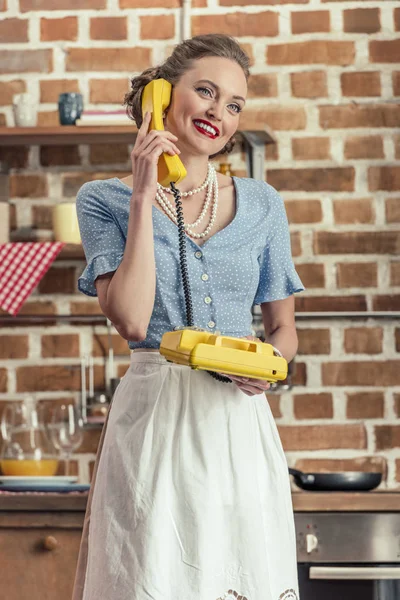 Красивая счастливая домохозяйка разговаривает по старинному ротационному телефону на кухне — стоковое фото
