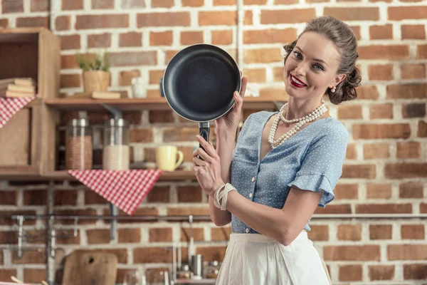 Belle femme au foyer souriante avec poêle à frire regardant la caméra à la cuisine — Photo de stock