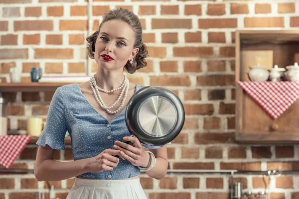 Attractive adult housewife with fryin pan looking at camera at kitchen — Stock Photo