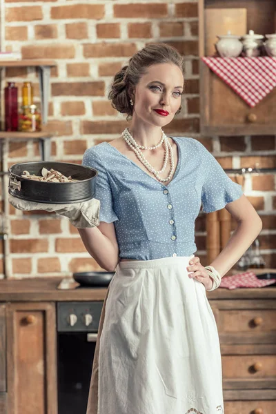 Beautiful adult housewife holding baking trey at kitchen — Stock Photo