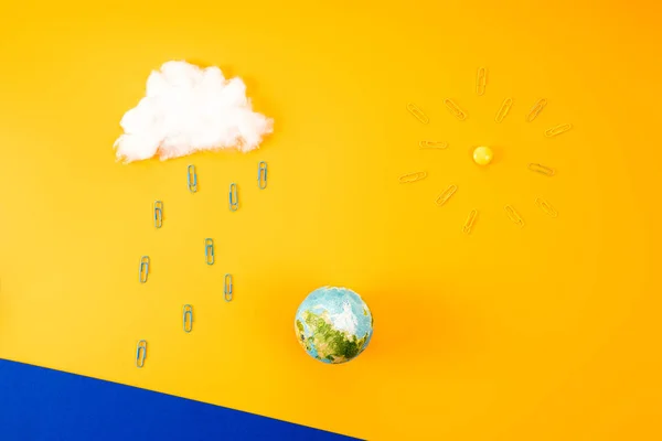 Top view of environment composition with earth globe and cloud with sun made of paper clips on yellow — Stock Photo
