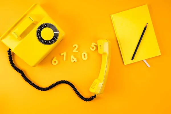 Вид зверху вінтажного телефону з блокнотом і номерами на жовтому — стокове фото