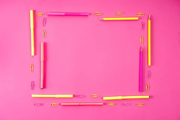 Vista superior del marco hecho de lápices, marcadores y clips de papel en rosa - foto de stock