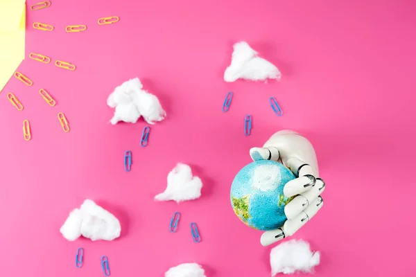 Top view of rain composition arranged of paper clips and cotton with robotic hand holding earth globe on pink — Stock Photo