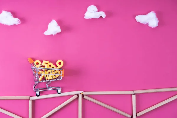 Shopping cart with numbers riding on bridge arranged with color pencils on pink — Stock Photo