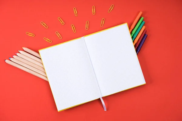 Flat lay with opened blank notebook with paper clips, color pencils and markers on red — Stock Photo