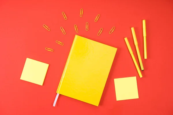 Flat lay with yellow notebook with supplies on red — Stock Photo