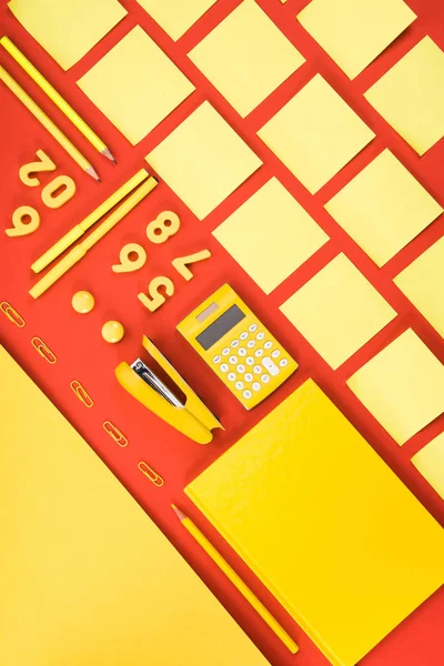 Disposición plana con suministros de escolarización amarillo arreglado en filas en rojo - foto de stock