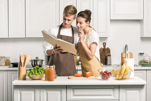 Joven pareja cocina ensalada y mirando libro de cocina en la cocina - foto de stock
