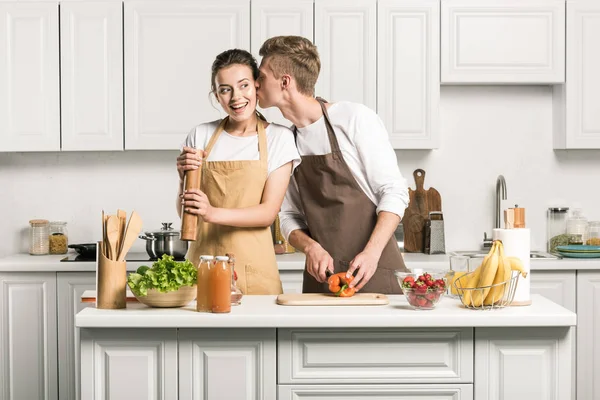 Хлопець цілує дівчину під час приготування салату на кухні — стокове фото