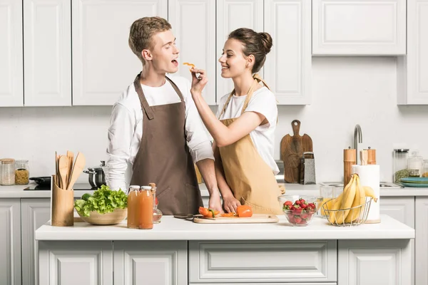 Girlfriend feeding boyfriend with piece of bell pepper in kitchen — Stock Photo