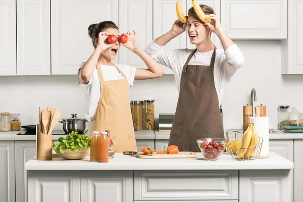 Jovem casal se divertindo com bananas e tomates na cozinha — Fotografia de Stock