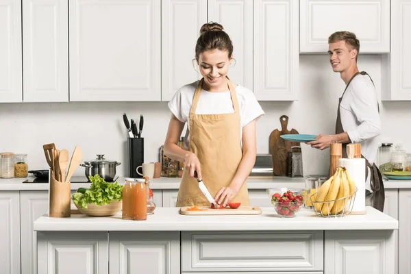 Girlfriend cooking salad and cutting tomatoes in kitchen — Stock Photo