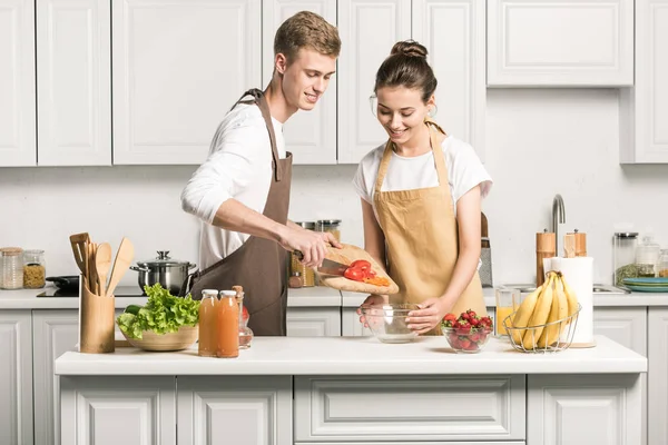 Jeune couple cuisine salade et mettre des légumes sains dans un bol dans la cuisine — Photo de stock