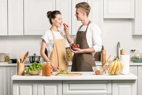 Novio alimentación novia con fresa en cocina - foto de stock