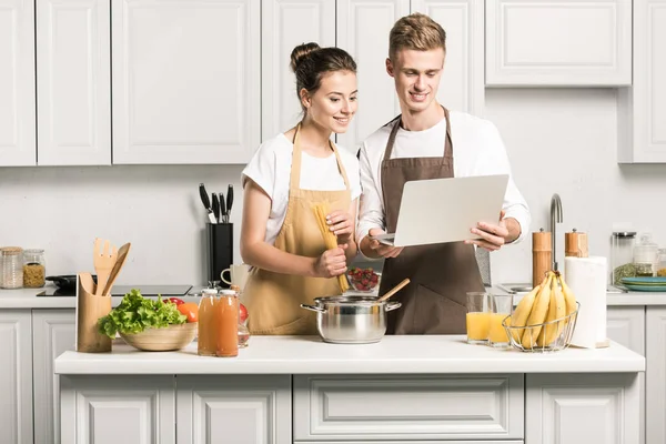 Young couple cooking pasta and using laptop in kitchen — Stock Photo