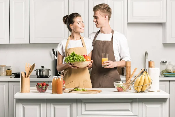 Jovem casal segurando legumes e copo de suco na cozinha — Fotografia de Stock