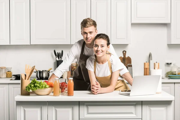 Молодая улыбающаяся пара смотрит в камеру на кухне — стоковое фото