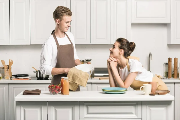 Namorado secando pratos na cozinha, namorada olhando para ele — Fotografia de Stock