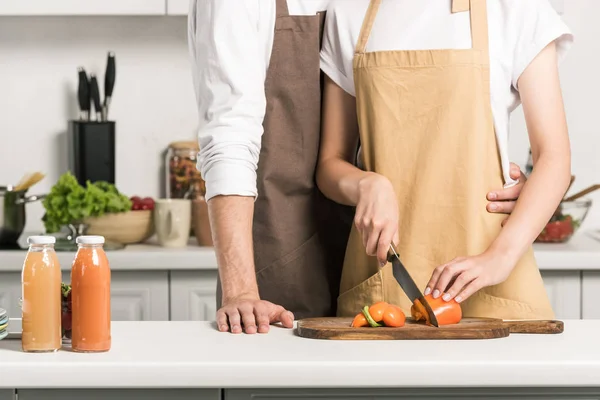 Cropped image of couple cooking salad and cutting tomatoes in kitchen — Stock Photo